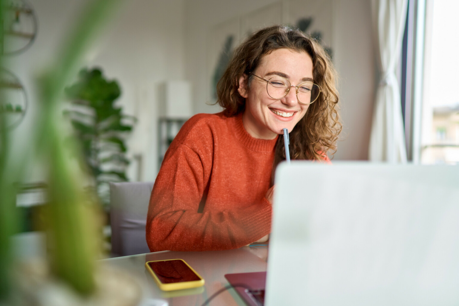 Happy young woman using laptop sitting at desk writing notes while watching webinar, studying online, looking at pc screen learning web classes or having virtual call meeting remote working from home.